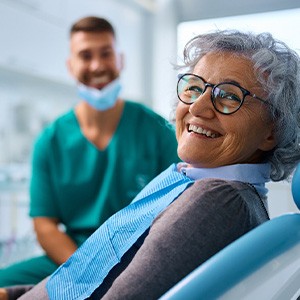 Woman with black glasses smiling while sitting in treatment chair
