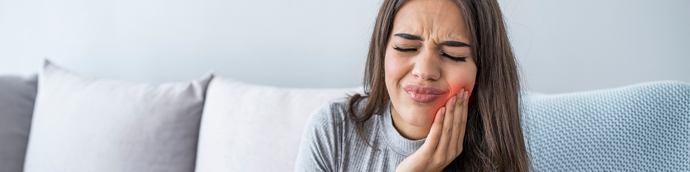Woman sitting on couch rubbing jaw in pain