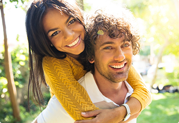 Smiling man giving smiling woman a piggyback ride
