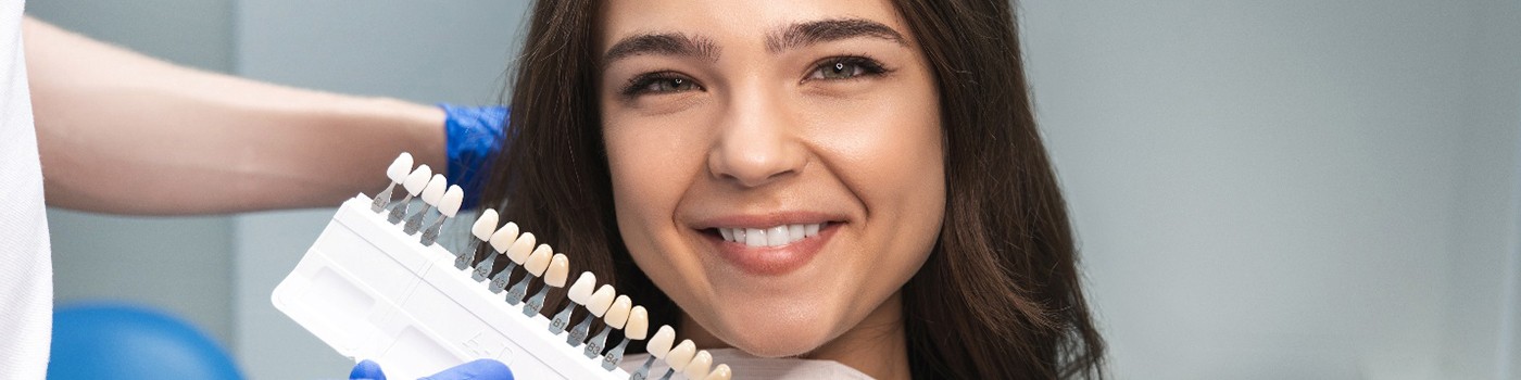 Woman gesturing to shade guide held close to her smile