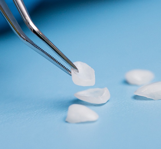 Closeup of forceps grasping veneers from light blue surface